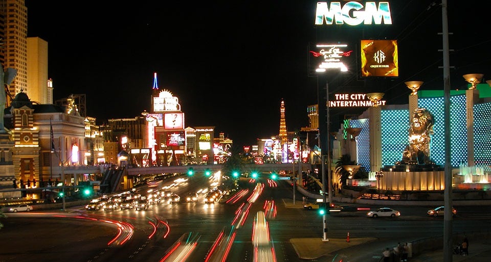 A late night street view of the Las Vegas Strip, with car lights and resort signs shining.