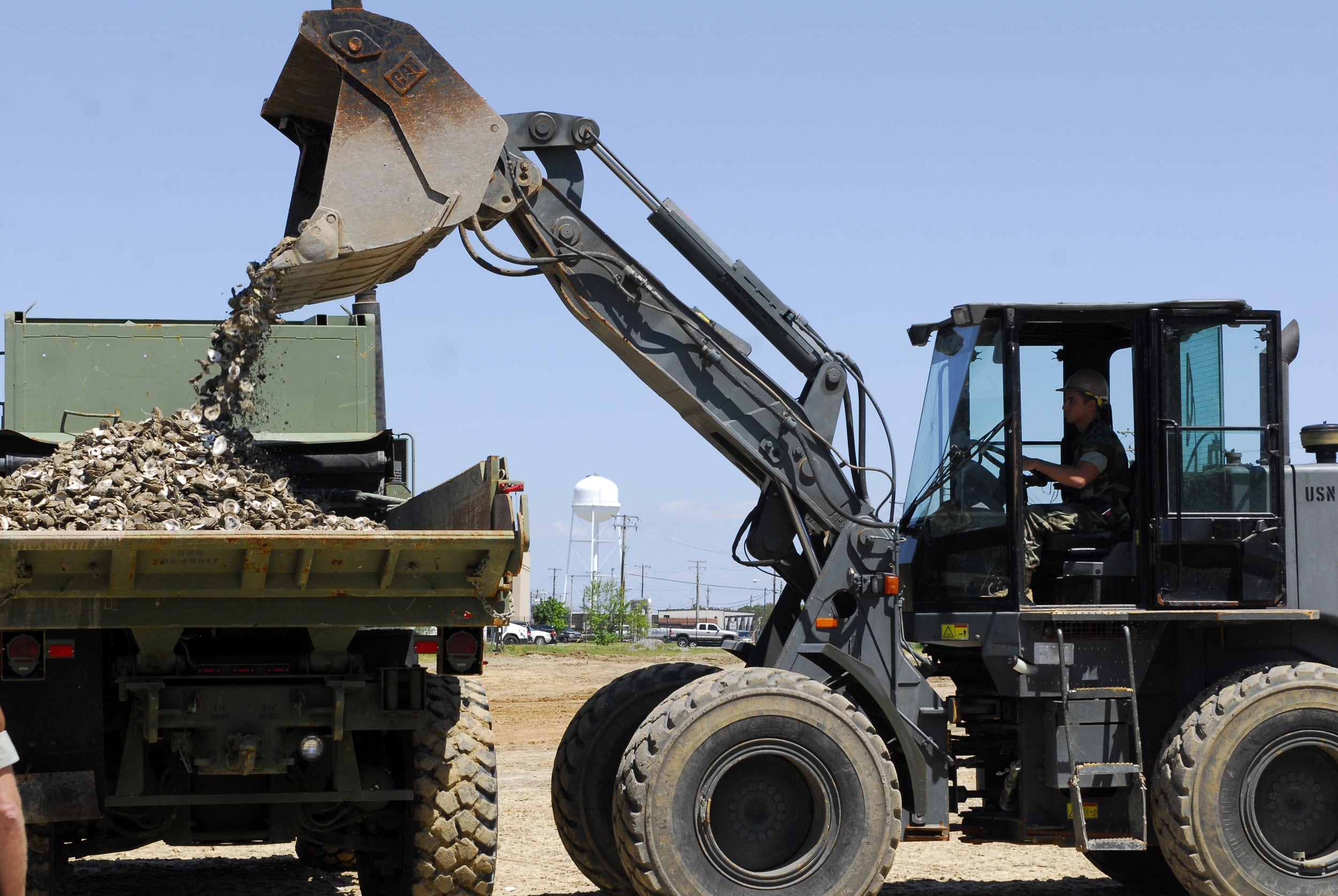 A front Loader dumps debris into another truck.