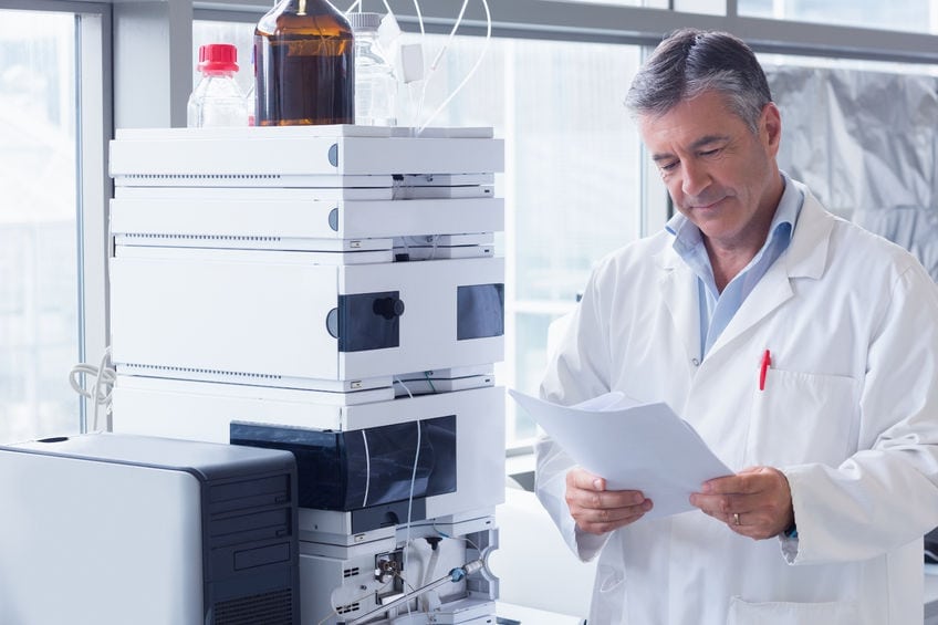 A scientist standing in a lab coat reads an analysis in a laboratory